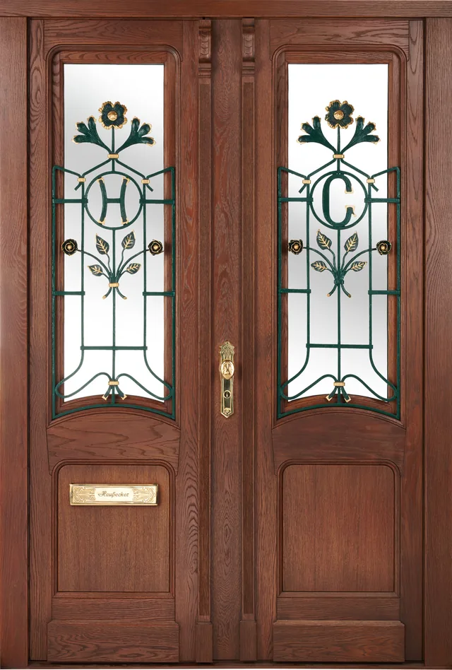 Zweiflügelige Haustür aus Eiche mit geschmiedeten Ziergittern vor dem Glas, in die die Initialen H und C mit Blüten und Blattwerk eingearbeitet sind